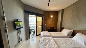 Habitación de hotel con dos camas, un televisor montado en la pared, una silla y vistas de la ciudad a través de una puerta de vidrio.