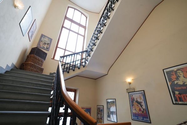 A staircase with a wooden handrail and black metal balusters, leading to a landing with framed pictures and posters on the walls. - Villa Borghese House (Rome)
