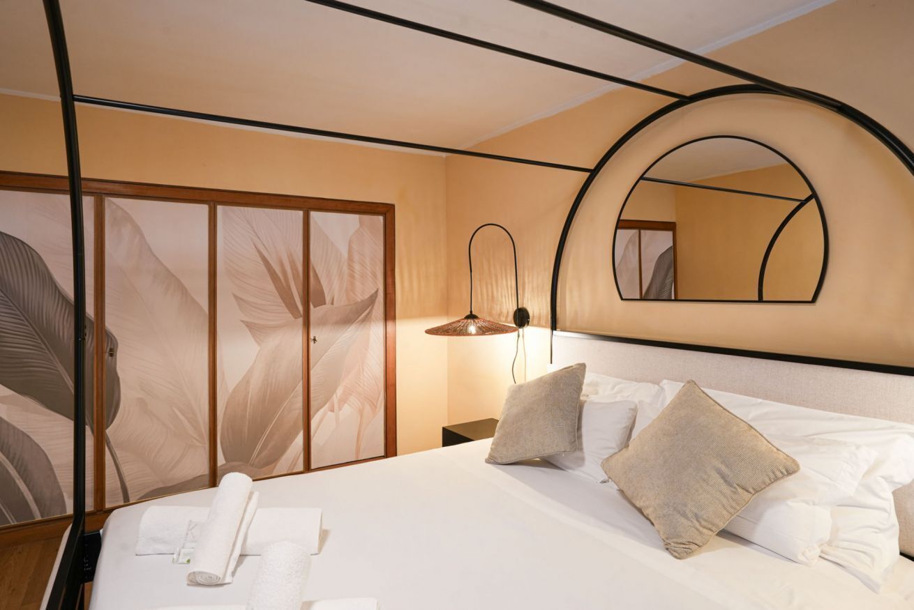 A hotel room with a bed, a nightstand, a lamp, a mirror, and a wardrobe.