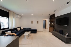Ein modernes Wohnzimmer mit einer Eckcouch, einem Couchtisch, einem Flachbildfernseher an einer dunklen Wand und einem Bücherregal.