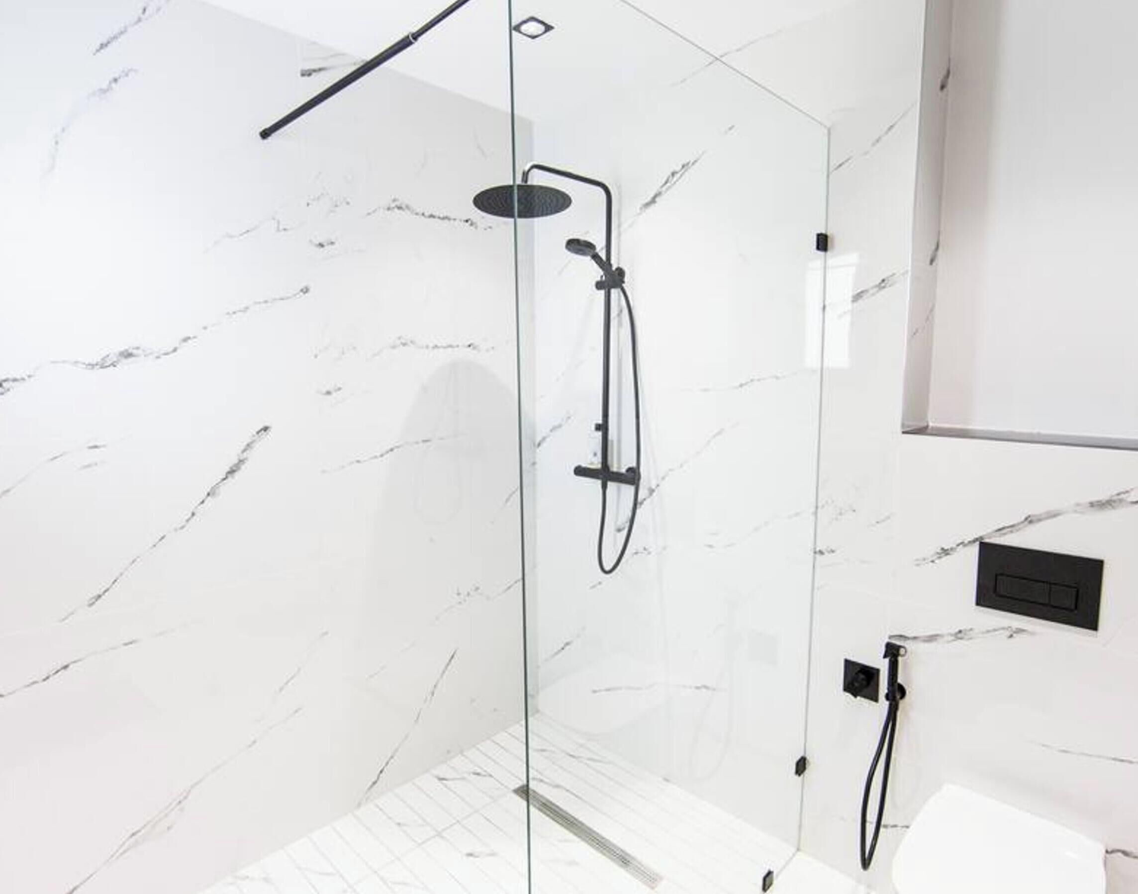 Ein modernes Badezimmer mit einer gläsernen Duschkabine, Marmorwänden und einem minimalistischen Design.