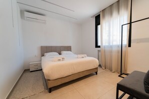 A clean, modern bedroom with a bed, bedside tables, an air conditioning unit, a window with curtains, and a small seating area. - Sunset 205 Luxury 1bd with gym (Tunis)