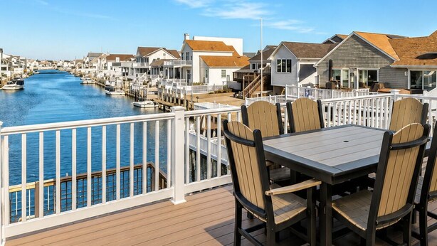 A deck with a table and chairs overlooking a marina with boats and houses. - Waterfront Lagoon Escape , Sunset Views, Private Dock and Minutes to LBI (Stafford Township)