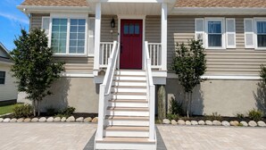A two-story house with a red front door, white railings, and a small porch. - Waterfront Lagoon Escape , Sunset Views, Private Dock and Minutes to LBI (Stafford Township)