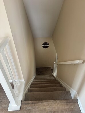 Una escalera con alfombra y barandillas blancas, un letrero de bienvenida circular y una pared lisa.