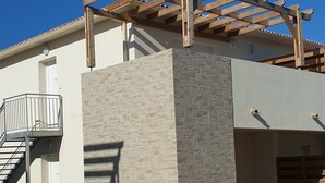 Un edificio moderno con fachada de piedra, una pérgola de madera y un sendero de hormigón.