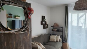 Un salón con un espejo rústico, un sofá gris, un estante negro pequeño y un ventanal grande.