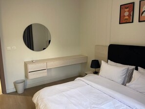 Ein Schlafzimmer mit einem Bett, einem Nachttisch, einer Lampe, einem Spiegel, einem Wandregal und einem Mülleimer.