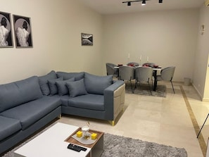 Ein modernes Wohnzimmer mit einem grauen Ecksofa, einem weißen Couchtisch und einem Essbereich mit grauen Stühlen und einem Tisch.