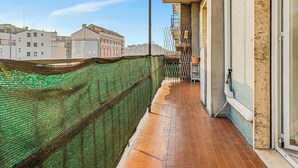 Un balcón con vistas a edificios, una cerca de malla verde y un piso de baldosas.