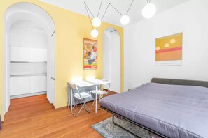 Ein Schlafzimmer mit einem Bett, einem Schreibtisch mit Stühlen, einem weißen Kleiderschrank und einem Bild an der Wand.