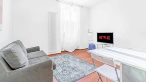 Un salon moderne avec un canapé gris, une table blanche et un téléviseur affichant le logo « NETFLIX ».