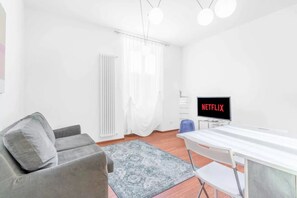 Ein modernes Wohnzimmer mit einem grauen Sofa, einem weißen Tisch und einem Fernseher, der 'NETFLIX' anzeigt.