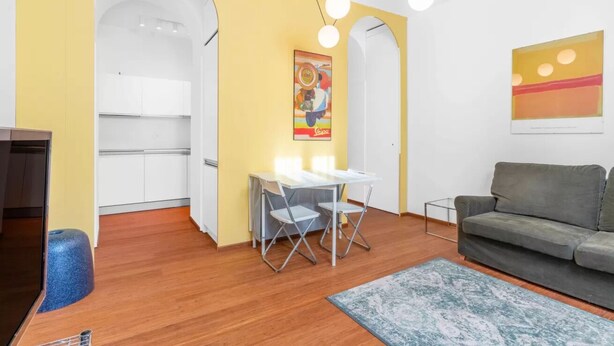 Un espace de vie compact comprenant un coin repas, un canapé et une cuisine visible à travers une arche.