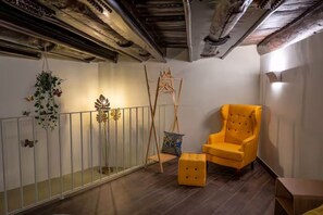 Ein Zimmer mit einem gelben Sessel, einem kleinen Hocker, einer dekorativen Stehlampe und einer hängenden Pflanze.
