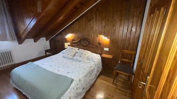 Um quarto acolhedor com teto de madeira, uma cama com colcha florida, duas luzes na parede e uma cadeira de madeira.