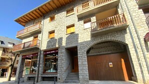 A stone building with a wooden balcony, a shop with a sign, and a large wooden door. - Benasque Shelter (Benasque)