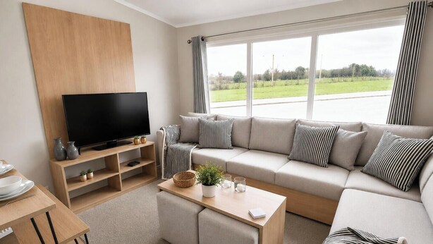 Ein modernes Wohnzimmer mit Flachbildfernseher, einem beigefarbenen Sofa, einem Couchtisch und einem großen Fenster mit Blick auf eine grüne Landschaft.