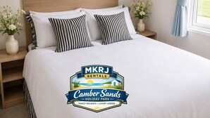 Ein Schlafzimmer mit einem großen Bett, zwei Nachttischen, einem Fenster mit Vorhängen und dem Logo von MKRJ Rentals.