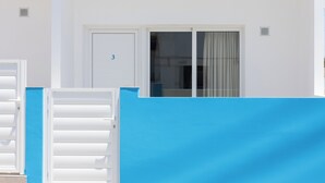 Un edificio blanco con un portón azul, una puerta con el número 3 y una ventana con cortinas.
