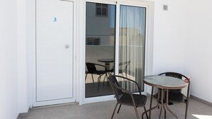 Un balcón con puerta corrediza de vidrio, una mesa y dos sillas.