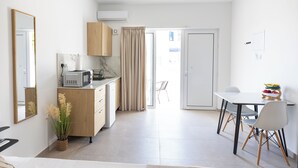 Cocina compacta con microondas, un refrigerador pequeño y un armario de madera. Hay una mesa de comedor con sillas y un frutero.