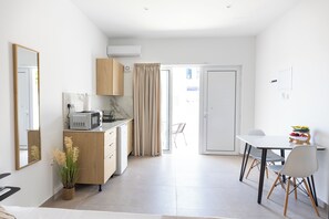 Eine kleine Küche mit Mikrowelle, einem kleinen Kühlschrank und einem Holzschrank. Ein Esstisch mit Stühlen und eine kleine Obstschale sind ebenfalls vorhanden.