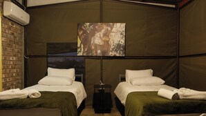A room with two beds, a brick wall, an air conditioning unit, and a painting on the wall.