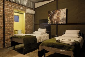 A hotel room with two beds, a brick wall, an air conditioning unit, and a painting on the wall.