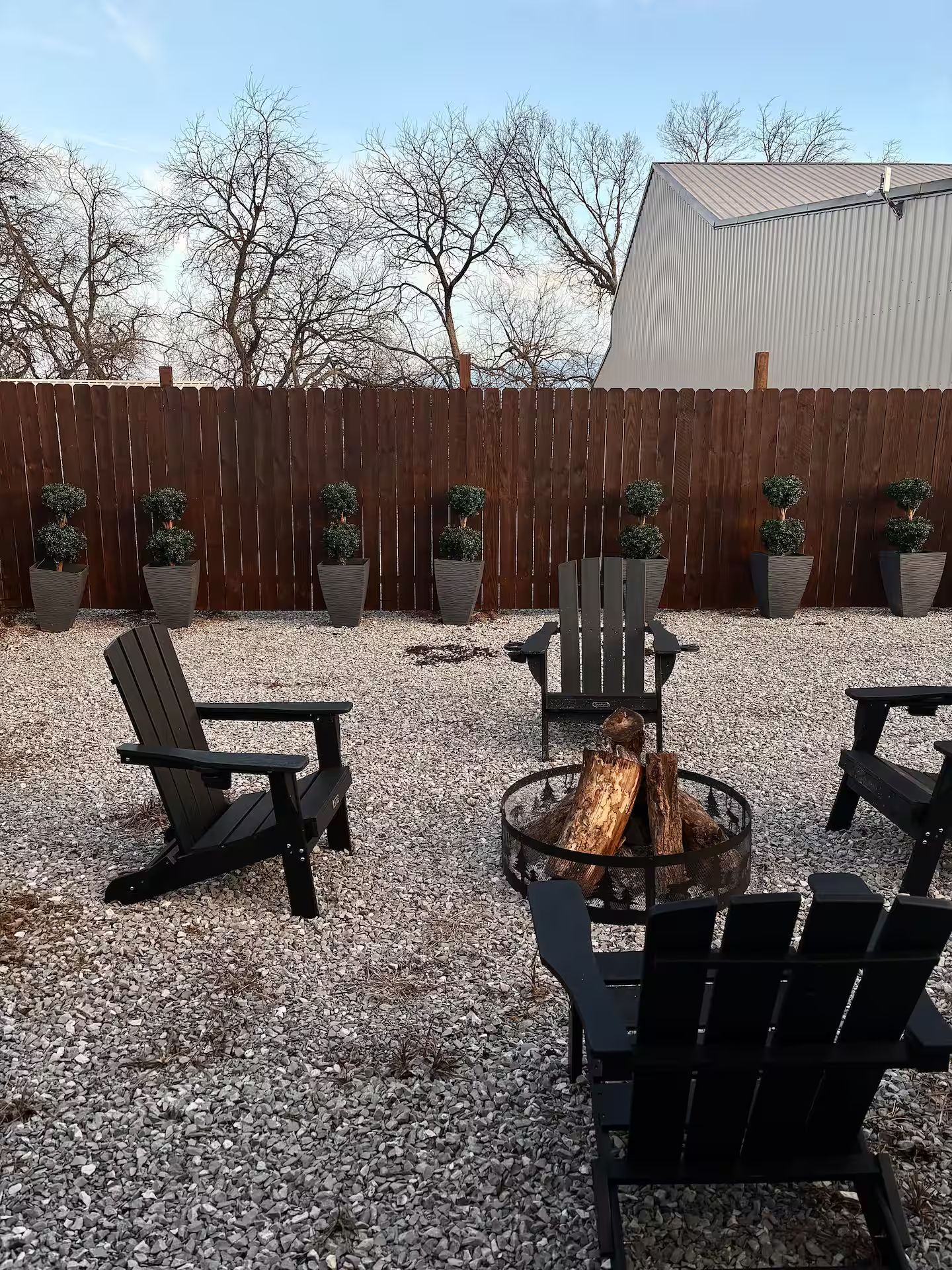 An outdoor seating area with Adirondack chairs, a fire pit, and potted plants.