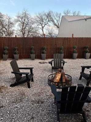 An outdoor seating area with Adirondack chairs, a fire pit, and potted plants.