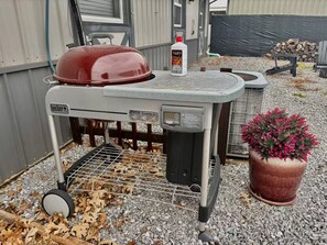 Een draagbare Weber barbecue met een digitale thermometer, een rode pan erop en een bloempot ernaast.