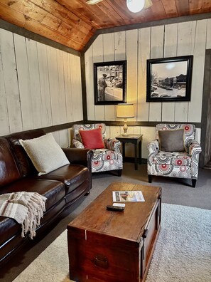Een gezellige woonkamer met een bruine leren bank, gestreepe fauteuils, een houten salontafel en een ingelijst schilderij aan de muur.