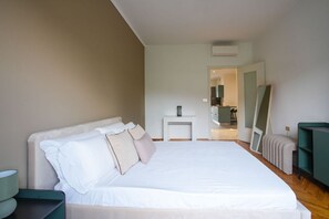 A bedroom with a bed, a nightstand, a mirror, and a green chair. - Torino Centro | Casa Valdocco (Turin)