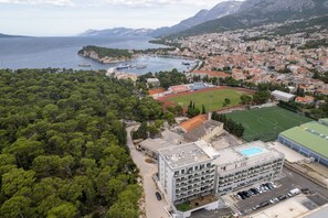 A coastal town with a sports field, a multi-story building with a rooftop pool, and a dense forest area.