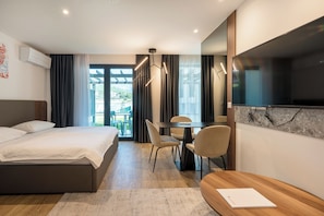 A modern hotel room with a bed, a desk with chairs, a television, and a view of the outdoors.