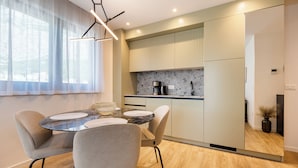 Una cocina moderna con una isla integrada, un área de comedor con una mesa redonda y sillas, y un ventanal con cortinas translúcidas.