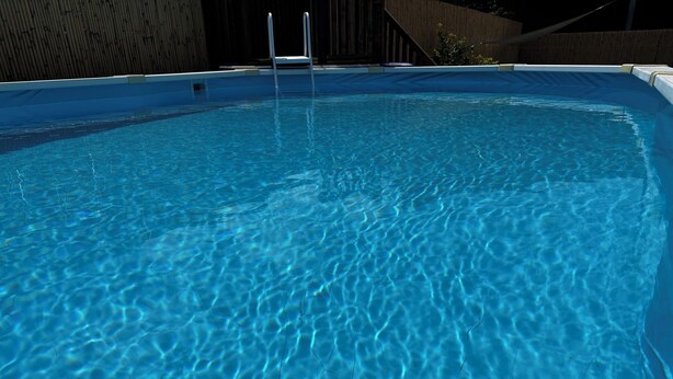En klar, blå swimmingpool med en træterrasse hele vejen rundt.