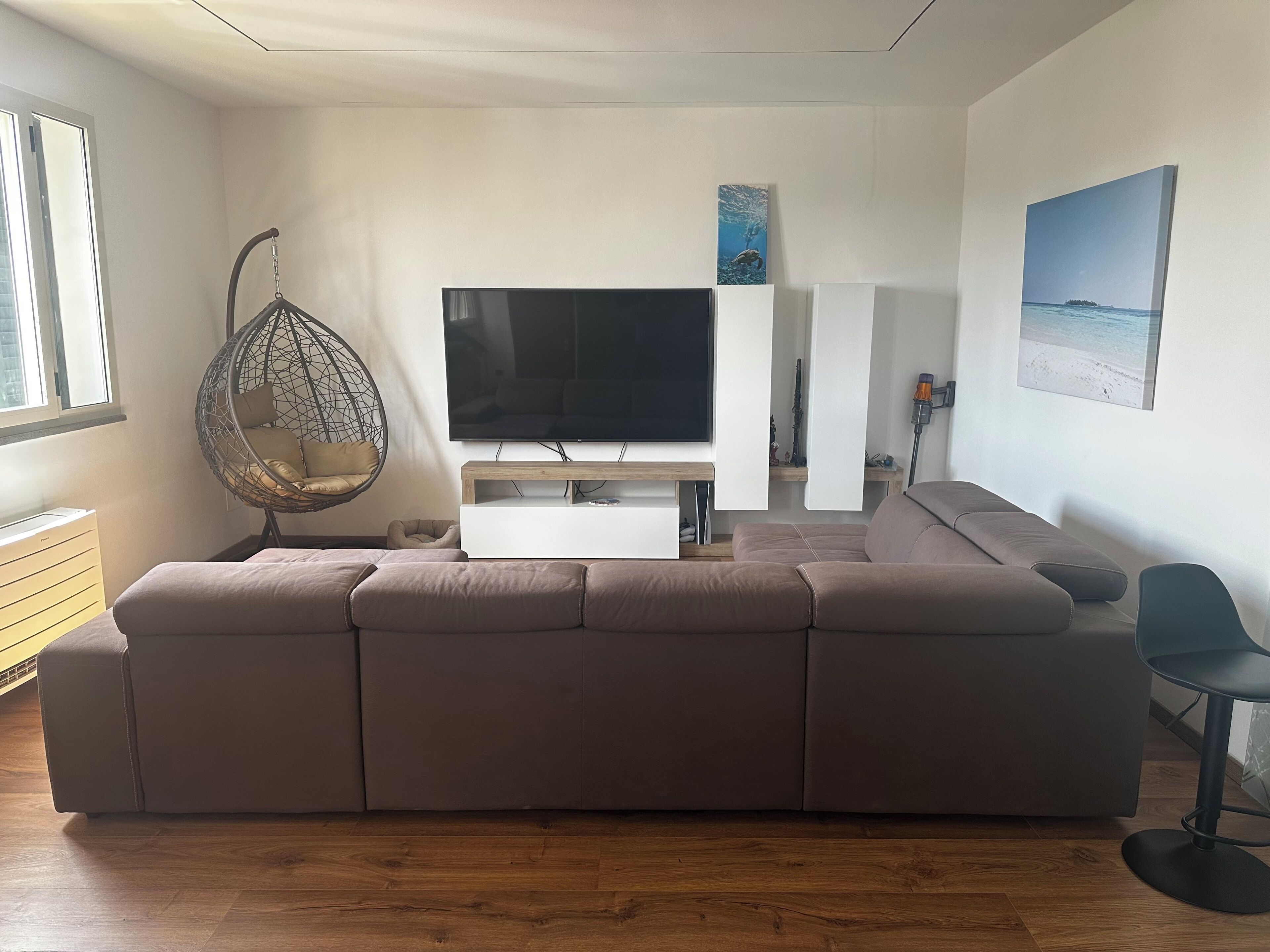 Een moderne woonkamer met een grote hoekbank, een hangstoel, een flatscreen televisie en kunstwerken aan de muur.