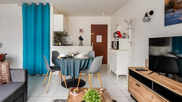 Ein modernes Wohnzimmer mit Essbereich, einem Fernseher und einer Küche im Hintergrund.