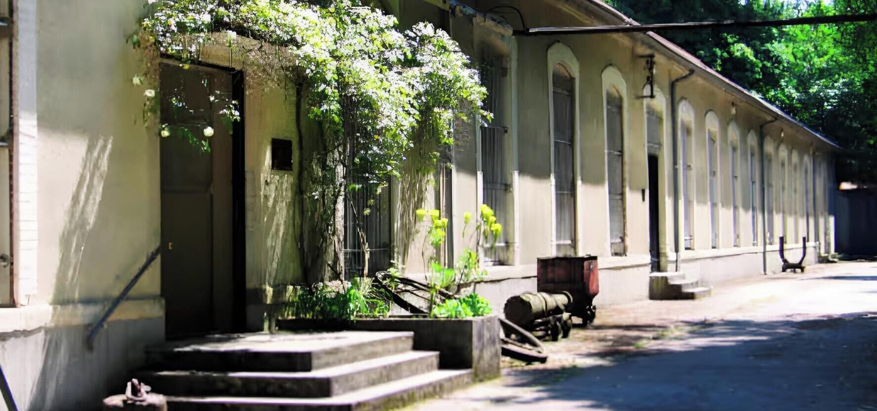 A building with a series of arched windows, a staircase leading to the entrance, and a parked vehicle.