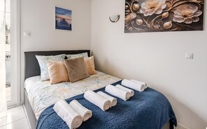 A neatly made bed with a floral bedspread, a dark headboard, and rolled towels on a blue blanket. - Cozy Studio - CDG - Exhibition Center - ARENA Grand Paris (Sevran)