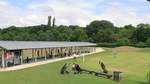 Ein überdachter Pavillon, ein kleines Gebäude mit roter Fassade und eine Rasenfläche mit Golfcarts und Taschen.