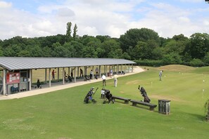 A covered pavilion with a roof, a small building with a red facade, and a grassy area with golf carts and bags. - Cozy Studio - CDG - Exhibition Center - ARENA Grand Paris (Sevran)