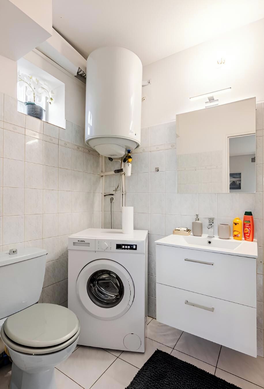 Ein modernes Badezimmer mit Waschmaschine, Toilette und Waschbecken, ausgestattet mit Pflegeprodukten.