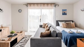 Ein modernes Schlafzimmer mit einer Couch, einem Bett, einem Schreibtisch und einem Fenster mit Vorhängen.