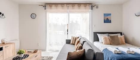A modern bedroom with a sofa, a bed, a desk, and a window with curtains.