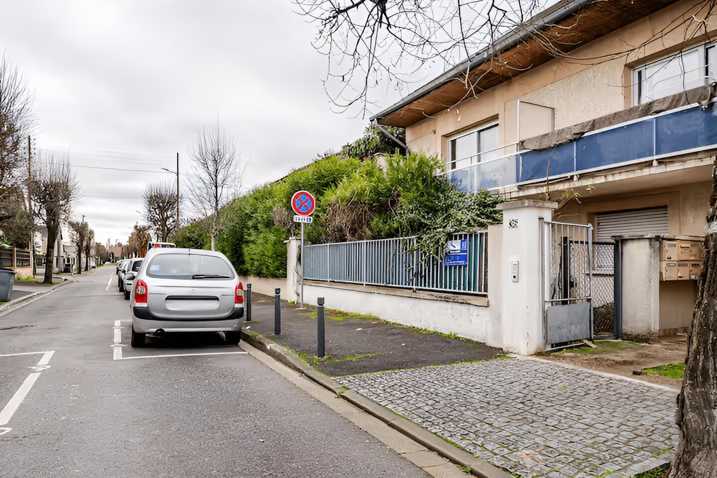Een woonstraat met geparkeerde auto's, een parkeerverbod en een hek bij de ingang van een gebouw.