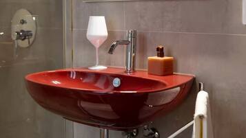 Un lavandino da bagno rosso con un moderno rubinetto, un bicchiere e un dispenser di sapone.