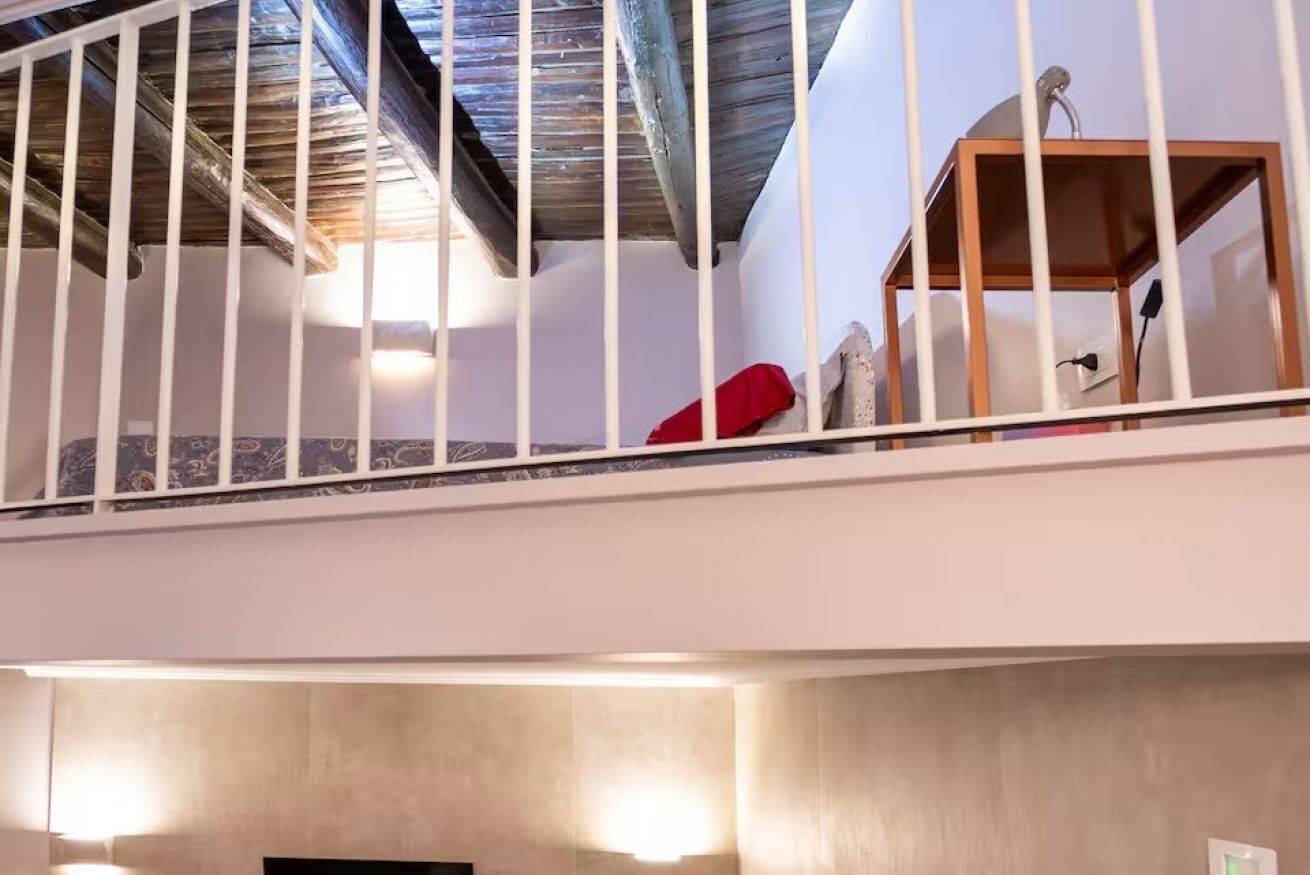Una stanza con soffitto alto, travi a vista, struttura in legno e un oggetto rosso sul pavimento.